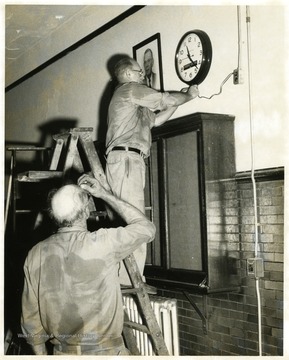 View of two workmen hanging a clock in Morgantown Jr. High School on Spruce and Walnut Streets.