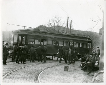 Men surround streetcar off the track.