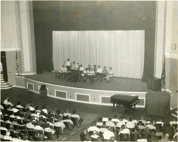 Group seated on the stage of the Morgantown High School auditorium before a audience.