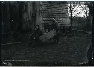 View of a man in a wheelbarrow being pushed past a barn in Morgantown, W.Va.