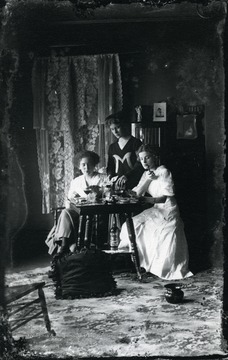 One woman appears to be smoking a pipe, another a cigarette while playing cards and drinking wine.