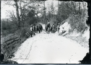 Men and two boys working on a country road with mallets.