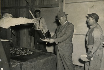 Men stand in line with their paper plates for a serving of grilled meat.