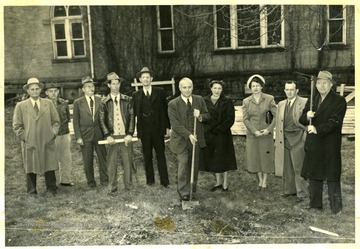 people gather to watch a man with a shovel head the groundbreaking ceremony.