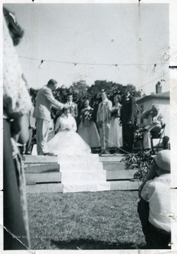 Woman sits as a man places a crown on her head.