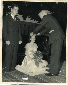 Woman sits as a man places a crown on her head.