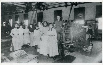 Interior view of the S. George Paper Factory showing eight female employees standing with one male.  An African-American woman is seated near the printing press.  