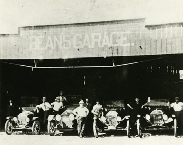 Group of men stand beside vehicles at Bean's Garage in Moorefield, West Virginia. 'Bean acquired a Ford dealership in Moorefield in 1910.'