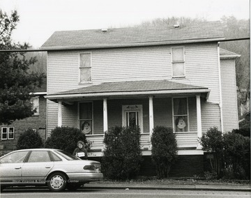 Women stands outside a home next to a car.  