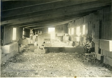 'Interior of scratching room of the T shaped house. This room is 14'6" x 80'. Note nest boxes, home-made hoppers, sliding windows, and water pans. Mr. Stone is sitting on a box to the right.' From photo album labeled 'Stewart A. Cody, County Agent, Jackson County, 1912.'