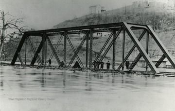 Men and boys standing on a bridge barely above flood waters.  Photograph given to Dr. Core by Mrs. A. C. Shively. 