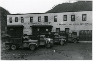 Two unidentified men pose in front of the Service Department International Trucks - Automobiles Light and Heavy Trucks