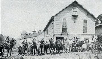 Crew with horses standing in front of the barns.