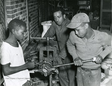 A scene of three African American boys putting some equipment into a vice at the West Virginia Industrial School for Colored Boys.
