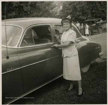 Photograph of Helen Ballard Clark standing next to a car.