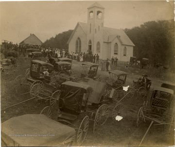 A view of the Mt. Hedding Methodist Church in Lillydale. A large crowd of people gather for the service with their carriages parked on the lawn in the foreground.