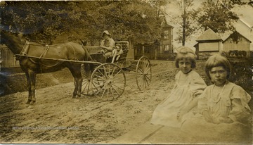 Collie Everman sits in a buggy with 'Dan'. Maggie and Helen Ballard sit at the side of the road in the foreground.