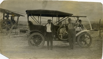 Two men stand in front of an automobile while 'Uncle Sim Ballard is in the background, all dressed up'.