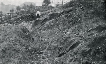 Geological Survey.  Man stands near a cut in the hillside.