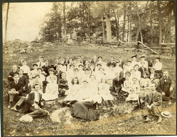 'Rocky Point Academy, Sinks Grove, Monroe County, West Virginia. Professor Lacey-front far right, behind Lacey's left shoulder-Charles Alexander Keadle.  Photo from home of C. A. Keadle; Pictured are Olive Leland Steele with hat with stripes and Eva B. Steel in front of her? Center right back man in button up coat is Robert Morton Steele.  Ray P. Beckett back with face half hidden.  Also pictured Miss Trimbil, music teacher front, center.'