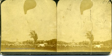 Two views of a crowd watching a balloonist just above the tree top.