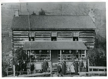 Family portrait in front of John M. Ruddle Home, built in 1871 in Buffalo Hills near Ruddle, W. Va.  Pictured left to right: John Preston, Lelia, Aud, John M., Ernest, Virginia F. Ruddle, Zola Simmons, Almeda Ruddle Simmons and Floyd Ruddle.  Portrait in frame is deceased son Tyree Bruce Ruddle.