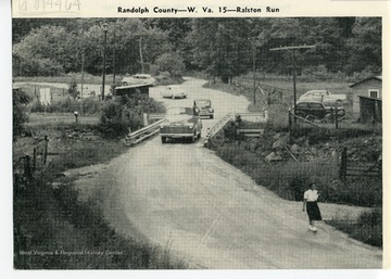 A view of automobiles on W. Va 15, Ralston Run.  Lady walking in front.  Randolph County, W. Va.