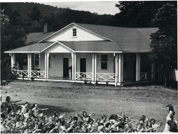 Front view of the dining hall in Camp Lightfoot with children pictured on grass in front of building.