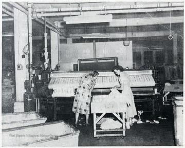 Two women stand at the ironing machine.