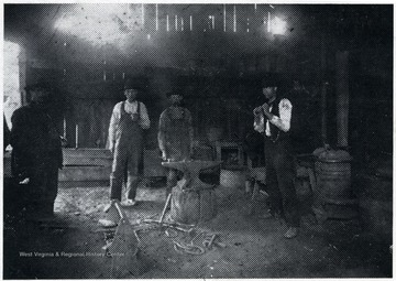 Four men stand around an anvil in the blacksmith shop.
