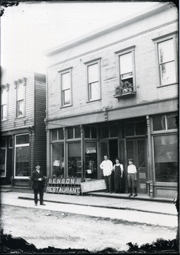 View of man on sidewalk and man, woman, and child on steps of Benson's Restaurant.  Signs read 'Pop on ice, soda water, &amp; ice cream. The Terra Alta Candy Co's Ice Cream for sale here'