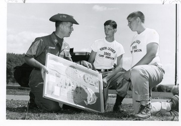 Two youth leaders are looking at a display held by U.S. Air Force Serviceman Stewart at Camp Dawson in Preston County, West Virginia.