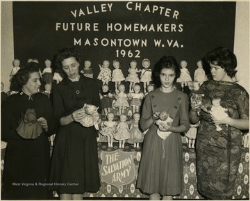 Members of the Valley Chapter Future Homemakers holding dolls and standing in front of a doll display.