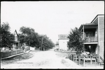 There is a wooden sidewalk on the left of the picture.  There is also a woman sitting on a porch on the right of the picture.