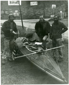 Three men pose with a kayak.
