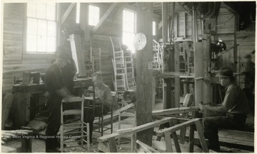 The men work in a wood shop building chairs.