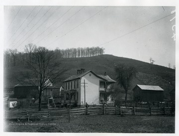 A view of a farm house and two other buildings behind a wooden fence.