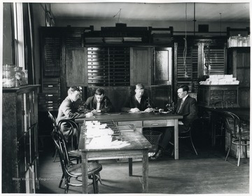 The four men are writing notes at a table with microscopes.