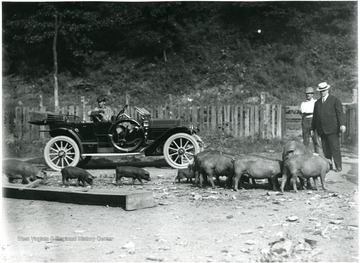 An early model automobile, possibly a Ford, is parked in front of the fence.