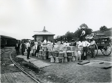 Group of men and women standing with baskets in front of freight station building.