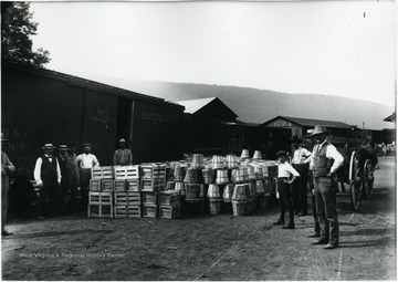 Men standing in front of train cart with barrels of peaches.