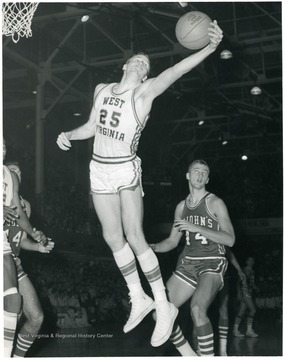 West Virginia University Basketball player, Bob Benfield, number 25, in mid air, reaches for a rebound in a game against St. Johns. 