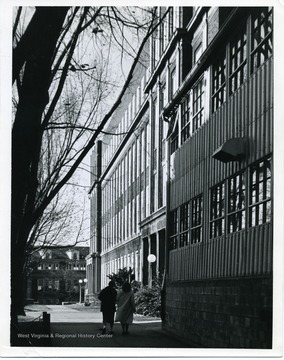 Two students are walking on the sidewalk by the 'Tin Can' temporary Engineering Building and Clark Hall, West Virginia University.