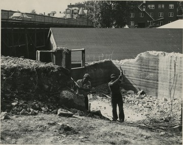 View of two men working on Plant Pathology Greenhouse.  Old stadium bridge pictured in background.