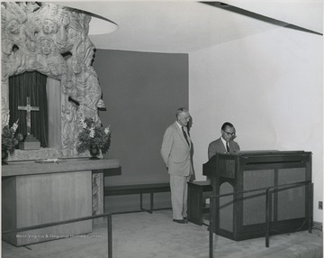 View of two men at chapel in Medical Center.  Dr. Clyde English pictured at organ.