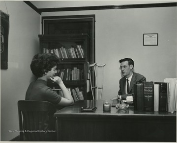 View of woman at man's desk at Student Health, now known as the Carruth Center.
