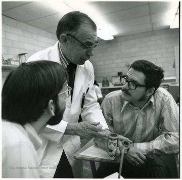 Man in the white coat (possibly Homer Patrick)speaking with two male students.