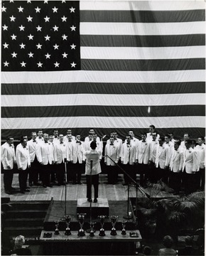 Choir singing in front of a large American flag.
