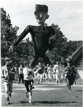 Cheerleaders and the Mountaineer lead the WVU Football team into the stadium through a massive Mountaineer figure. 