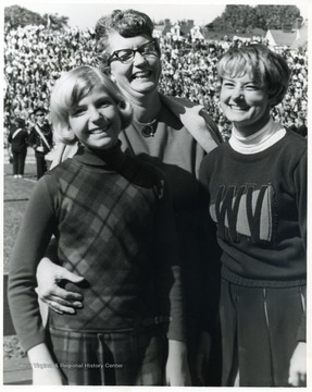 Mother standing behind two daughters, one is a cheerleader, at Mountaineer Field.